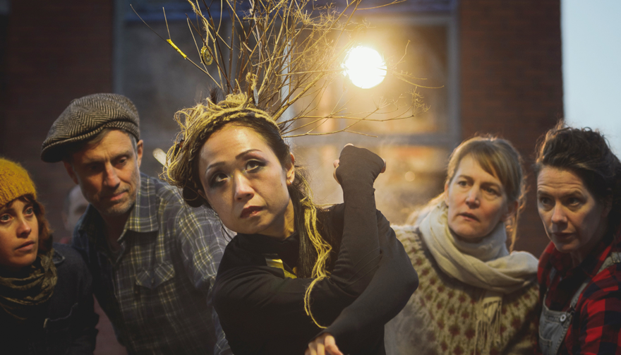 En grupp människor står på rad och tittar in i kameran. En stark lampa lyser i bakgrunden. En bild som syftar till att väcka uppmärksamhet och marknadsföra en föreställning.
