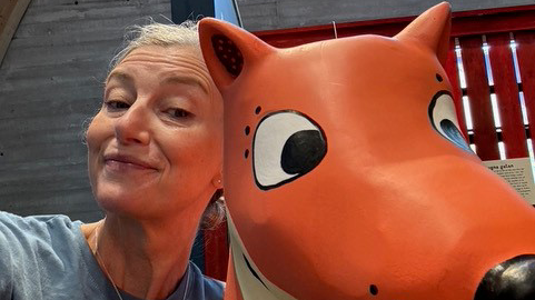 En kvinna står intill en tecknad rävskulptur.