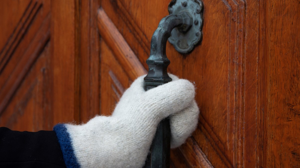 Bild på hand iklädd vante som tar tag i handtaget på en dörr